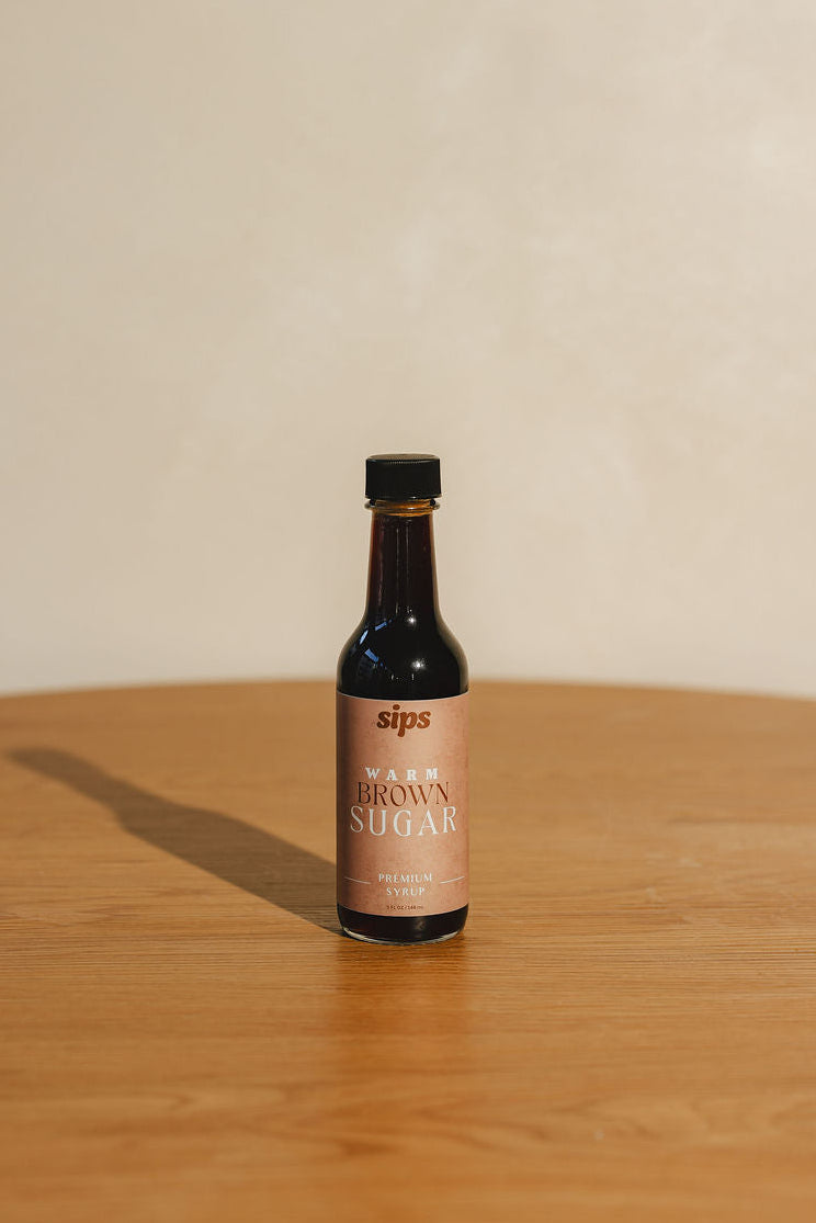 Bottle of Sips warm brown sugar syrup on a wooden surface with a beige background