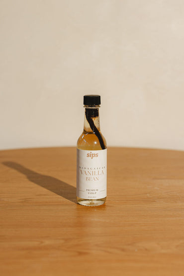 bottle of Sips Madagascar vanilla bean syrup on a wooden surface with a beige background